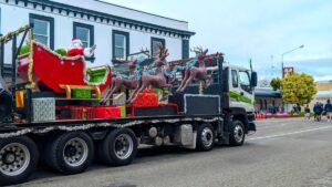 Nieuw-Zeelandse Kerst-optocht. Aankomst van de Kerstman, die met arreslee en rendieren op een vrachtwagen zit.