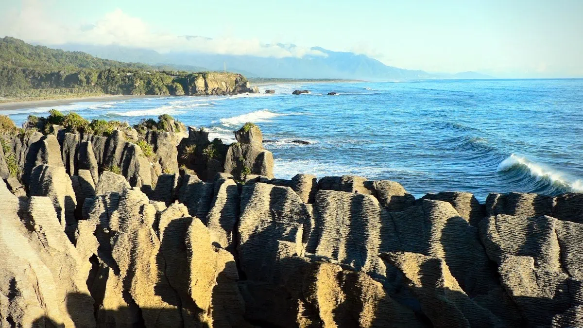 Pancake Rocks - kalksteenrotsen die op een stapel pannenkoeken lijft. De foto kijkt van bovenaf op de rotsen en langs de kustlijn.