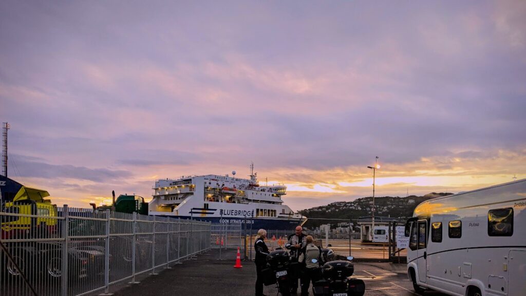 Zon komt op terwijl de reiziger wachten tot het boarden van de vroge ferry begint. Uitzicht op ferry met ervoor auto's, motoren en campers die wachten